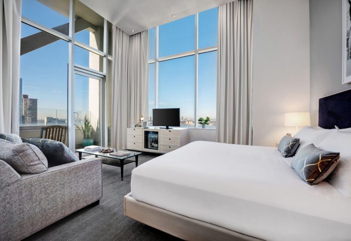 Ink 48 Hotel room. Gay-friendly hotel with city view, floor-to-ceiling windows, sofa, and king bed. Modern design for gay travelers.