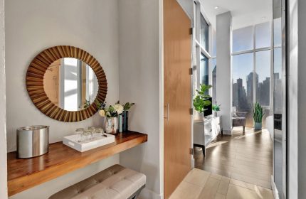 Ink 48 Hotel's gay-friendly room. A round mirror hangs above a wooden shelf with glasses, flowers, and an ice bucket. City view beyond.