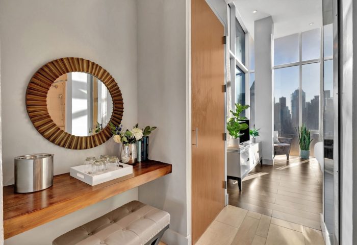 Ink 48 Hotel's gay-friendly room. A round mirror hangs above a wooden shelf with glasses, flowers, and an ice bucket. City view beyond.