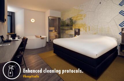 Inntel Hotels Amsterdam Centre room. Pet-friendly, gay-friendly hotel with a bed, bathtub, desk, and Amsterdam-themed wall. Enhanced cleaning protocols.