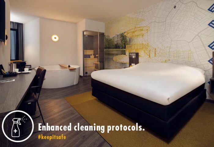 Inntel Hotels Amsterdam Centre room. Pet-friendly, gay-friendly hotel with a bed, bathtub, desk, and Amsterdam-themed wall. Enhanced cleaning protocols.