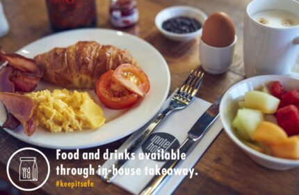 Breakfast at Inntel Hotels Amsterdam Centre, a gay-friendly, pet-friendly hotel. Croissant, eggs, bacon, fruit, and coffee on a wooden table.