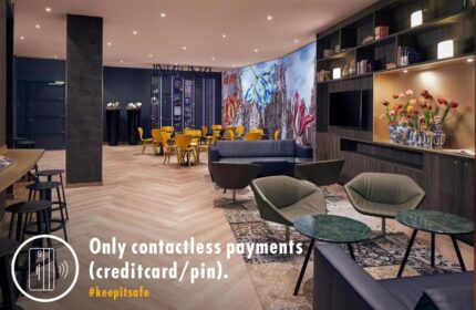 Inntel Hotels Amsterdam Centre lobby. Gay-friendly, pet-friendly hotel lounge area with seating, floral mural, and contactless payment sign.