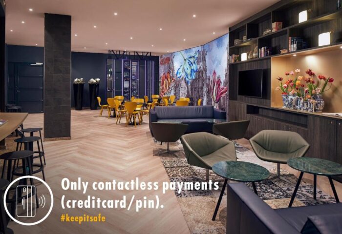 Inntel Hotels Amsterdam Centre lobby. Gay-friendly, pet-friendly hotel lounge area with seating, floral mural, and contactless payment sign.