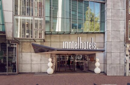Inntel Hotels Amsterdam Centre entrance. Gay-friendly, pet-friendly hotel with modern architecture. Tables and chairs in the foreground.