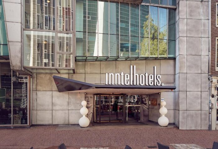 Inntel Hotels Amsterdam Centre entrance. Gay-friendly, pet-friendly hotel with modern architecture. Tables and chairs in the foreground.