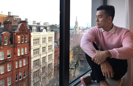 Gay man at Assembly Hotel, London. Stylish pink sweater, city view. Gay-friendly hotel inspiration for travel.