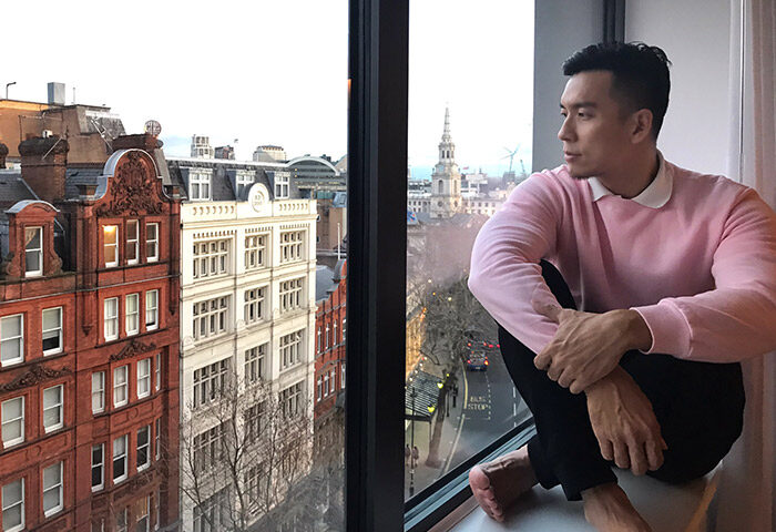 Gay man at Assembly Hotel, London. Stylish pink sweater, city view. Gay-friendly hotel inspiration for travel.