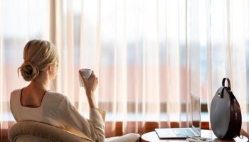 InterContinental Budapest: Woman enjoys coffee in a pet-friendly, gay-friendly hotel room. Laptop on table. Relaxing travel.