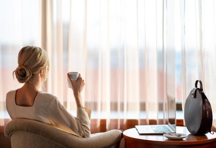InterContinental Budapest: Woman enjoys coffee in a pet-friendly, gay-friendly hotel room. Laptop on table. Relaxing travel.