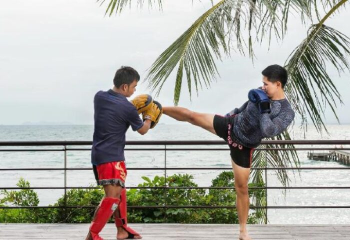 Muay Thai training at InterContinental Koh Samui Resort, a gay-friendly hotel. Man kicking pads, ocean view. Fitness and wellness for gay travelers.