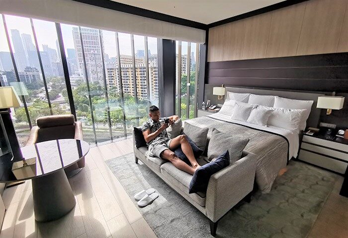 Gay-friendly InterContinental Singapore Robertson Quay hotel room. Man relaxing on sofa with city view. Luxury gay travel in Singapore.