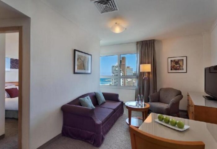Isrotel Tower Hotel room. Gay-friendly hotel suite with purple sofa, armchair, and city view. Modern design for gay travelers.