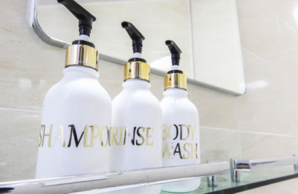 Bathroom amenities at Itaewon A One Hotel, a gay-friendly hotel. Shampoo, rinse, and body wash in white pump bottles on a glass shelf.