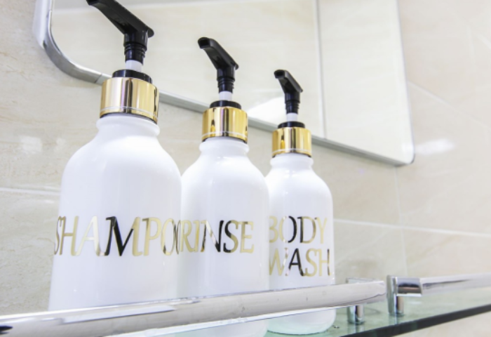 Bathroom amenities at Itaewon A One Hotel, a gay-friendly hotel. Shampoo, rinse, and body wash in white pump bottles on a glass shelf.