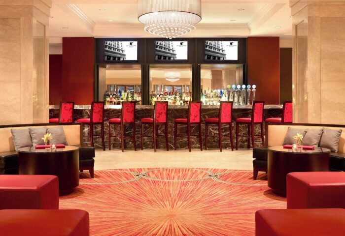 Bar at the gay-friendly JW Marriott Chicago hotel. Red chairs line the bar, with TVs above. Seating areas flank a patterned carpet.