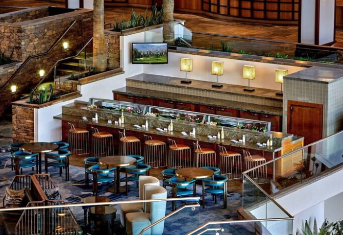 Interior of JW Marriott Desert Springs Resort & Spa, a gay-friendly hotel. Bar area with seating, tables, and stairs in a stylish setting.