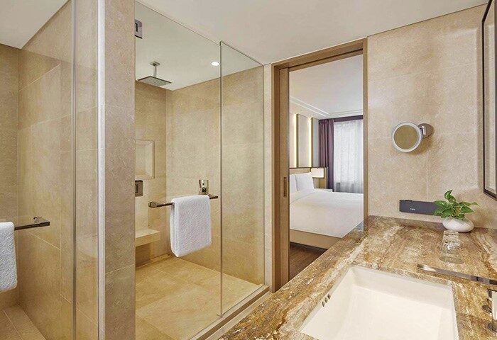 JW Marriott Hotel Seoul bathroom. Glass shower, marble sink, and view into bedroom. Gay-friendly hotel in Seoul, South Korea.