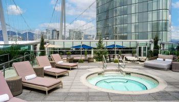 JW Marriott Parq Vancouver's outdoor pool area. This gay-friendly hotel features lounge chairs, a hot tub, and city views.