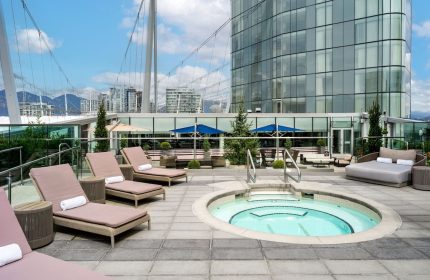 JW Marriott Parq Vancouver's outdoor pool area. This gay-friendly hotel features lounge chairs, a hot tub, and city views.