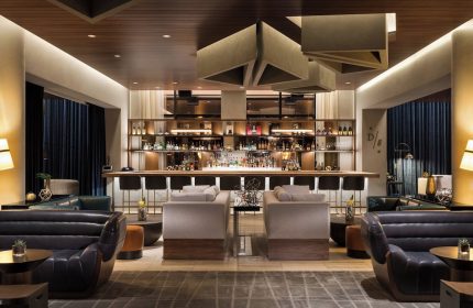 JW Marriott Parq Vancouver gay-friendly hotel bar area. Modern design with bar stools, lounge seating, and a fully stocked bar. Upscale ambiance.