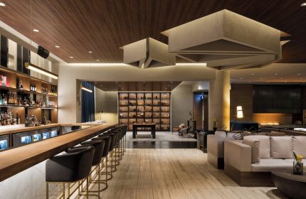 Interior of gay-friendly JW Marriott Parq Vancouver hotel. Bar with stools, lounge seating, decorative ceiling, and display case. Upscale design.