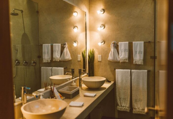 Bathroom at Gay-Friendly Jashita Hotel: Double sinks, towels with hotel logo, and modern lighting. Luxury travel for gay men in a stylish resort.