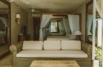 Jashita Hotel room: Wicker couch and table in front of a four-poster bed with white curtains. Gay-friendly hotel room with neutral tones.