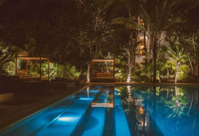 Jashita Hotel pool at night. Gay-friendly hotel with cabanas reflecting in the water. Tropical trees surround the luxury resort.