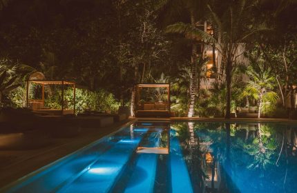 Jashita Hotel pool at night. Gay-friendly hotel with cabanas reflecting in the water. Tropical trees surround the luxury resort.