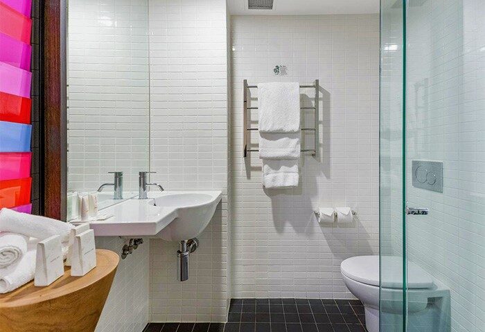 Bathroom at Jasper Boutique Hotel, a gay-friendly hotel. Features white tile, modern sink, glass shower, & black tile floor. Ideal for gay travel.