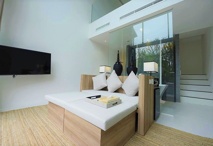 K Maison Lanna Boutique Hotel room. Modern design, white cushions, TV, and glass wall. Gay-friendly hotel in Chiang Mai, Thailand.