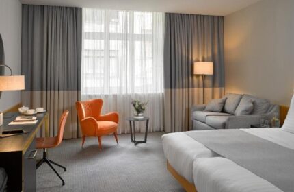K+K Hotel Fenix room. Gay-friendly, pet-friendly hotel. Room with bed, sofa, desk, chair, and orange armchair. Modern design. Window view.
