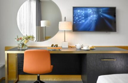 K+K Hotel Fenix room detail. Desk with orange chair, round mirror, and TV. Gay-friendly, pet-friendly hotel interior. Modern design.