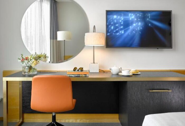 K+K Hotel Fenix room detail. Desk with orange chair, round mirror, and TV. Gay-friendly, pet-friendly hotel interior. Modern design.