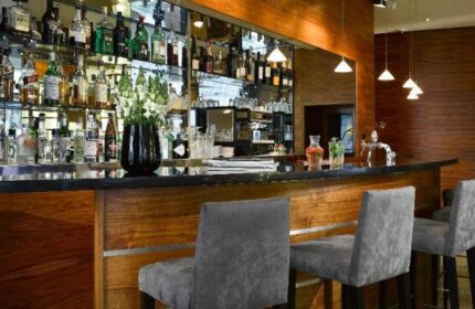 K+K Hotel Fenix bar area. Gay-friendly, pet-friendly hotel with a fully stocked bar, bar stools, and modern lighting. Wood and mirrored accents.