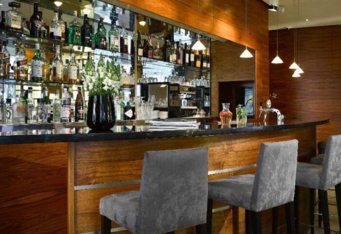 K+K Hotel Fenix bar area. Gay-friendly, pet-friendly hotel with a fully stocked bar, bar stools, and modern lighting. Wood and mirrored accents.