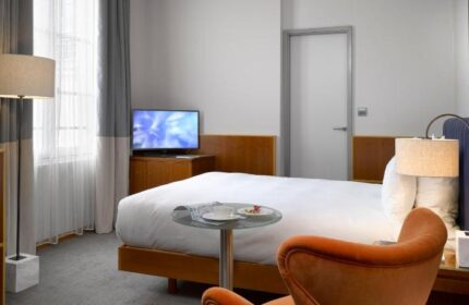 K+K Hotel Fenix room. Gay-friendly, pet-friendly hotel with modern decor. Bed, TV, chair, and lamp. A comfortable stay for gay travelers.