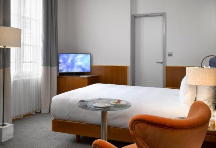 K+K Hotel Fenix room. Gay-friendly, pet-friendly hotel with modern decor. Bed, TV, chair, and lamp. A comfortable stay for gay travelers.