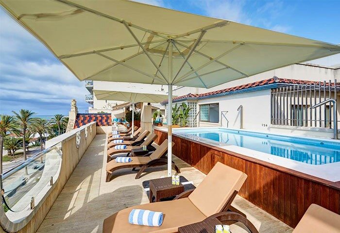 Kalma Sitges Hotel's gay-friendly rooftop pool. Lounge chairs line the deck, offering ocean views. A relaxing spot for gay travelers in Sitges.