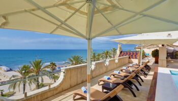 Kalma Sitges Hotel rooftop view. Gay-friendly hotel features beach views, sun loungers, and umbrellas. Ideal for gay travel in Sitges.