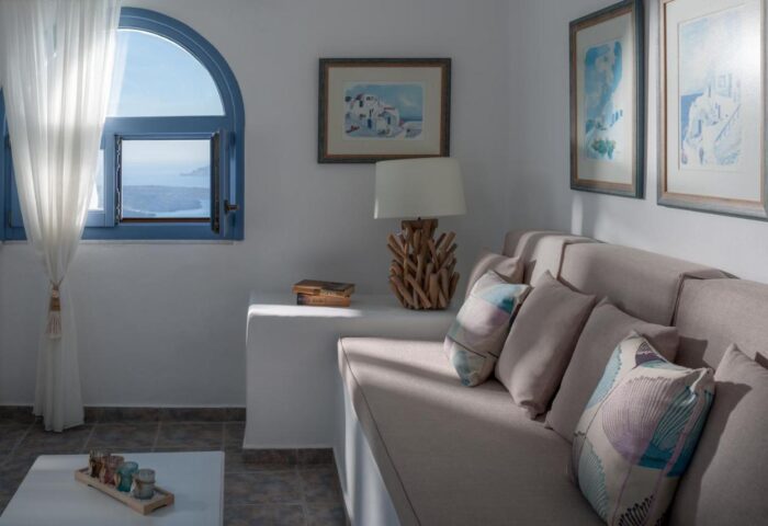 Kamares Apartments interior. Gay-friendly hotel room with sofa, pillows, lamp, and window view. Ideal for gay men's travel in Santorini.