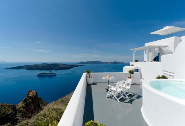 Kamares Apartments, a gay-friendly hotel. Balcony view of the Aegean Sea, cruise ship, and islands. White architecture, hot tub, and seating area.