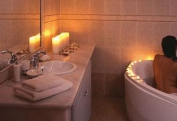 Kamares Apartments gay-friendly hotel bathroom. Man relaxing in a candlelit tub. Sink, towels, and romantic ambiance. Perfect for gay men's travel.