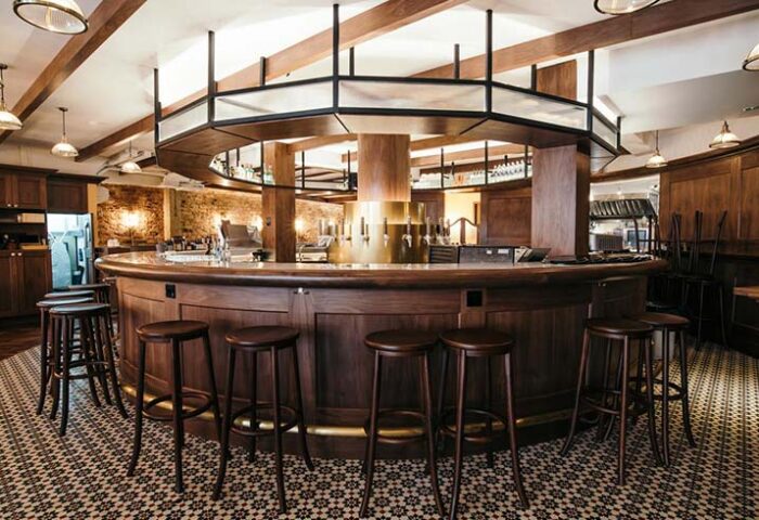 KēSa House, a gay-friendly hotel by Oakwood: interior view of the bar area with wooden stools and a circular bar, perfect for gay men travel.