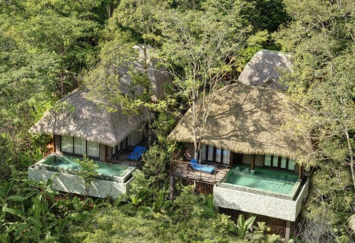 Keemala gay-friendly hotel aerial view. Thatched roof villas with private pools nestled in lush greenery. Perfect for gay men travelers' retreat.