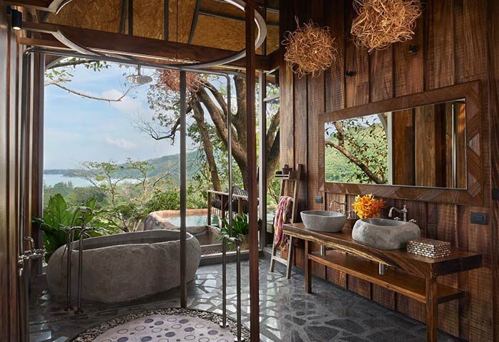 Keemala gay-friendly hotel bathroom. Stone bathtub & sinks, wooden walls, & jungle view. Luxury gay travel in Phuket, Thailand.