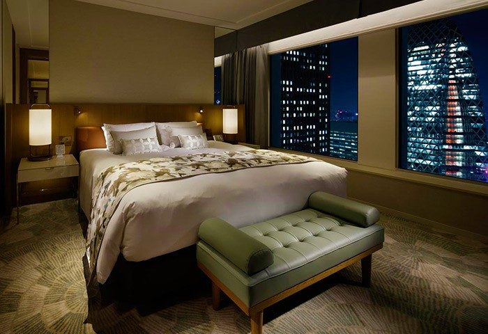 Keio Plaza Hotel Tokyo gay-friendly room at night. City view from window. Comfortable bed, bench, and modern decor. Tokyo gay travel.