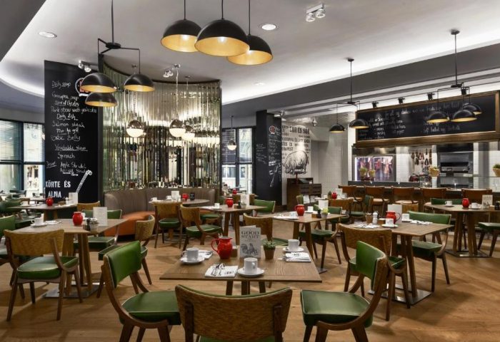 Kempinski Hotel Corvinus Budapest restaurant. Tables with green chairs, blackboards with menus. Gay-friendly, pet-friendly hotel dining.