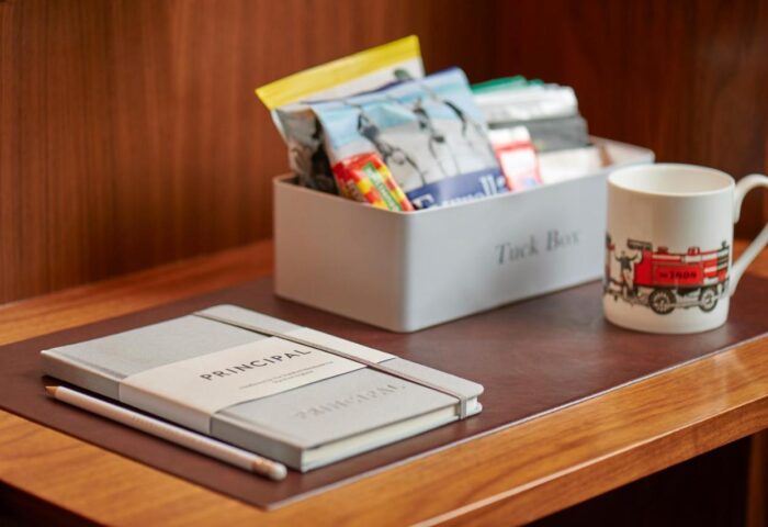 Kimpton Clocktower Hotel: Amenities on a wooden desk. Principal notebook, pencil, Tuck Box with snacks, and a mug with a fire engine.